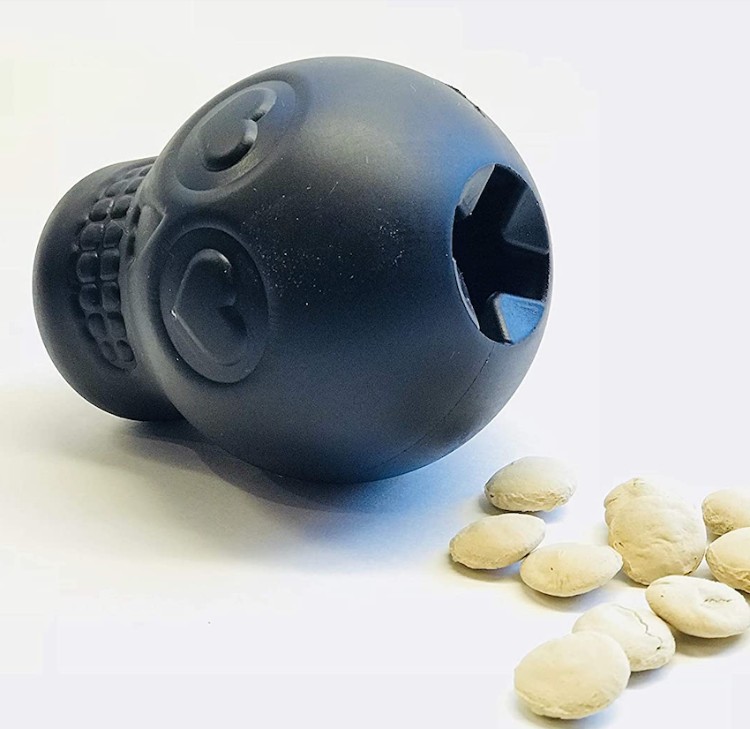 A black rubber skull shaped dog toy with some dog treats next to it
